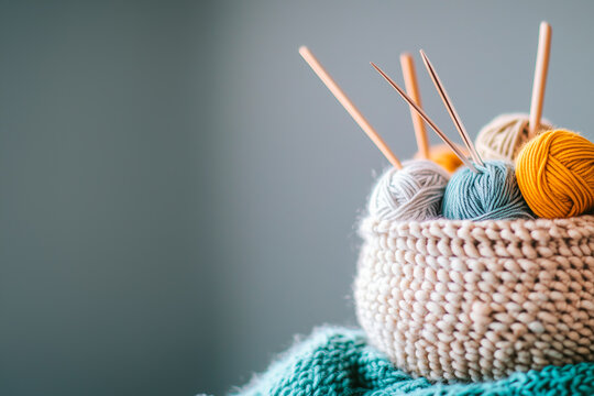  cozy basket filled with soft, colorful balls of yarn and a pair of knitting needles rests on a wooden surface. Perfect for crafting and showcasing creativity, banner, web, design, poster