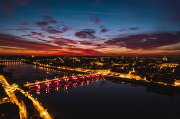 Obraz premium Colorful sunset casts a magical glow over the illuminated city and river at twilight