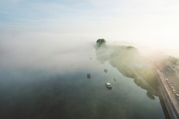 Misty morning blankets the tranquil river with soft reflections of boats and trees at dawn