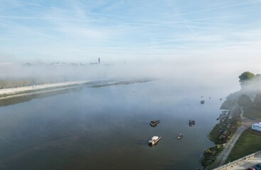Misty morning on the river with boats gliding through the soft fog under a clear blue sky in early dawn