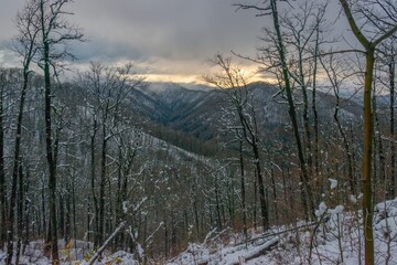 magnificent mountain landscape - dark low clouds with a gap over the snow-capped mountains of the Western Caucasus covered with forest on a winter day