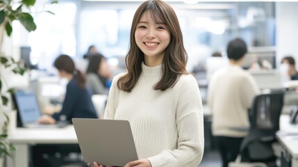 Smiling Japanese businesswoman standing in an office, holding her laptop. She is wearing casual clothes, and other people working behind her are blurred.,generated ai.	  