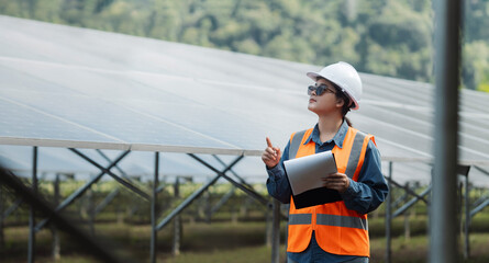 Female electrical engineer wearing hard hat inspecting solar farm panel equipment. Eco-friendly energy. Renewable clean energy technology concept.