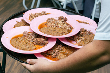 Waiter carrying plates with birria and refried beans. Mexican food.