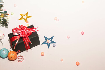 Obraz premium Season's greetings scene. Christmas decorations,gift boxes with red ribbons, сhristmas balls, rustic star, holly berries, frosty spruce branches, confetti on white backdrop, selective focus with blur