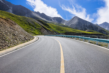 Naklejka premium Countryside asphalt road and green meadow with mountains nature landscape in Xinjiang. Beautiful scenery along the Duku Highway in China.