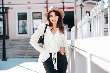 Portrait of young beautiful smiling hipster woman in trendy summer white blouse and jeans. Carefree woman posing in the street in sunny day. Positive model outdoors. Cheerful and happy