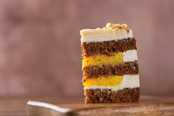 Piece of vegan pumpkin spice or carrot layered cake with coconut cream, walnut and orange confit on a brown background. Sugar, gluten and lactose free.