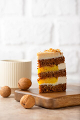 Piece of pumpkin or carrot cake with coconut cream, walnut and orange confit in a wooden board with cup of tea on a table. Sugar, gluten and lactose free. Vegan, healthy dessert. Vertical orientation.