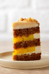 Piece of vegan pumpkin or carrot layered cake with coconut cream and orange confit on a light background. Sugar, gluten and lactose free. Vertical orientation, closeup.
