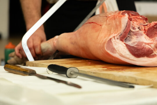 Butcher sawing through a pork leg on a wooden table during preparation