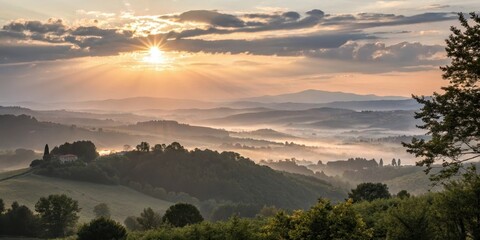 Obraz premium Sunrise over rolling hills, a tranquil morning mist veiling the landscape, and a solitary house nestled amongst the trees.