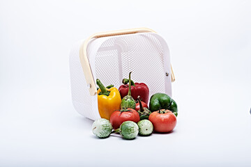 Basket with fresh vegetables and some fruit photographed on a white background