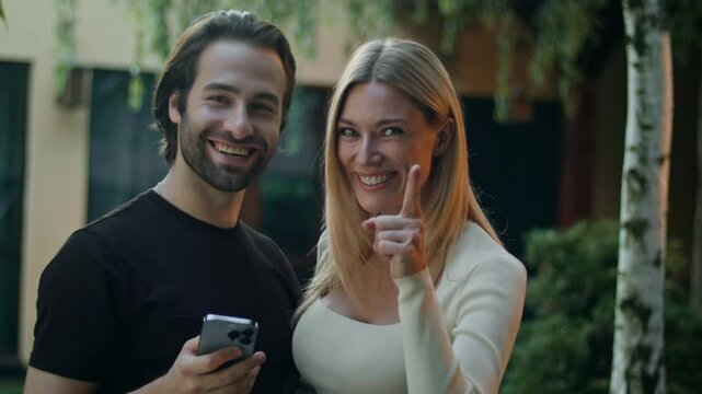 Standing outside, they tap the smartphone screen and win a prize on a mobile app. Man shows the green screen to the camera, proudly pointing at it, celebrating their big victory and success.