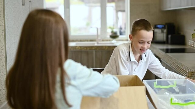 Child boy sort paper and plastic into separate containers in the kitchen at home. Sorting recycling items for plastic, paper and metal drop offs. Waste segregation, waste sorting, waste recycle.