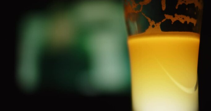 A brightly coloured glass of unfiltered beer against a TV screen in a darkened room