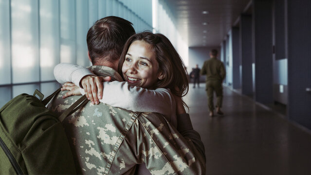 Joyful reunion in an airport hallway as a woman embraces her returning military partner.