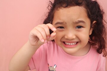 Asian female toddler smiling showing her missing tooth while holding her missing tooth close up.