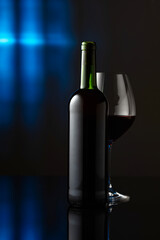 Glass and bottle of red wine on a black reflective background.