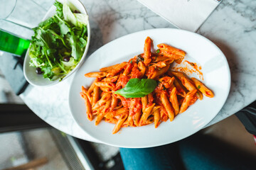 Delicious Italian Penne Pasta In Tomato Sauce Served With Fresh Green Salad On Marble Tabletop Perfect For Lunch Or Dinner Enjoyment In Authentic Restaurant Setting