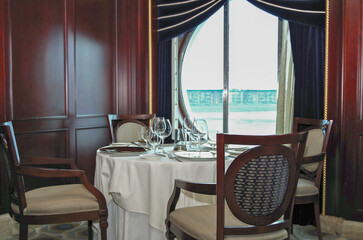 Formal and elegant ocean view Art Deco dining room restaurant onboard luxury cruiseship or cruise ship liner with set tables in classic interior design style and ceiling ambient lighting