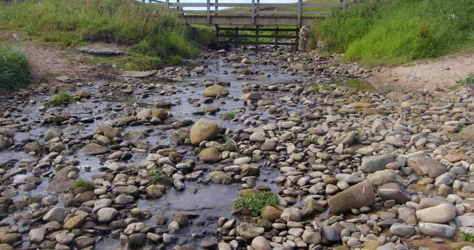 wide shot of a small stream entering the beach with a wooden bridge at Longhoughton beach of the howdiemony sands. Alnwick