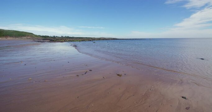 Extra wide shot of a sandy beach with a large boulder and waves rippling over it, at Longhoughton beach of the howdiemony sands. Alnwick.