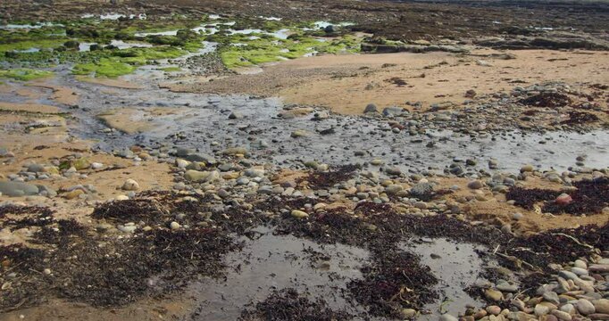 shot of a small stream flowing over sand and rocks enter the sea at Longhoughton beach of the howdiemony sands. Alnwick