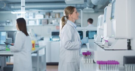 Team of Biomedical Engineers Work in a Lab. Senior Researcher Adding Samples to Test Machine, Asian Female Adjusting Settings on a Digital Microscope while Male Colleague Carrying Medical Glassware - Powered by Adobe
