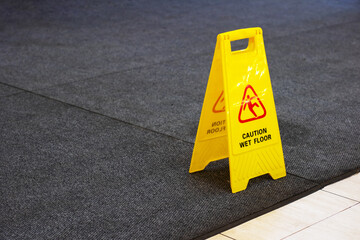 A bright yellow sign displays a caution notice about a wet floor