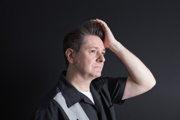 Man 50 years old with elegant shirt, touching his hair with toupee on black background. Studio shot. Concept of classic style and masculine sophistication