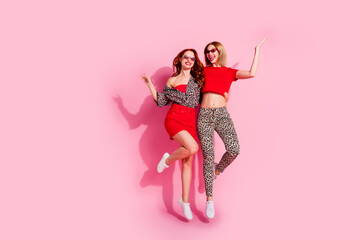 Full body photo of two attractive young women jump hugging have fun dressed stylish red leopard print clothes isolated on pink background