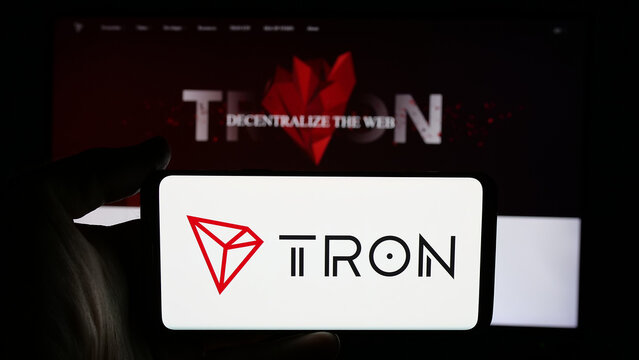 Stuttgart, Germany - 11-20-2024: Person holding cellphone with logo of decentralized blockchain TRON on screen in front of webpage. Focus on phone display.