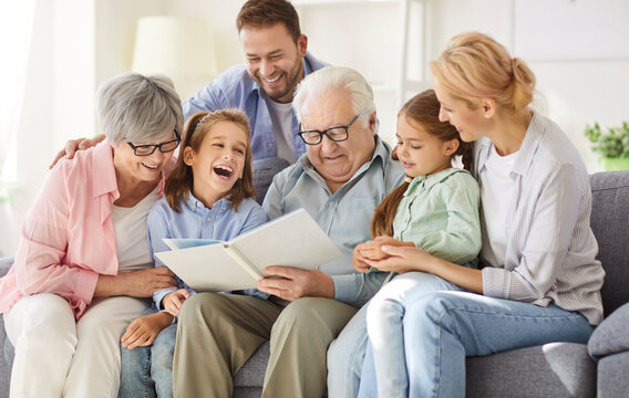 Happy big family, gathering at home on sofa, laughing three generations got printed album, viewing funny family life moments, enjoy photos remembering, photobook, parents, grandparents, children fun