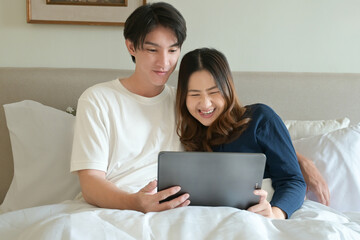 A man and woman are lying in bed together, with the man holding a tablet.