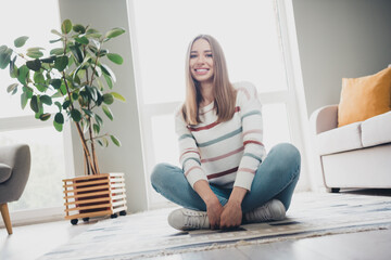 Cheerful young woman relaxing in modern living room with natural light and stylish decor, enjoying a peaceful weekend afternoon at home.