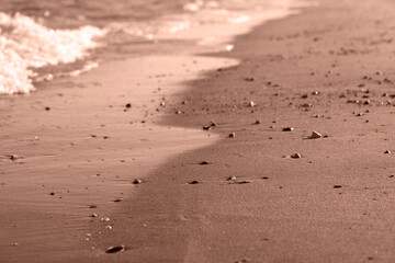 Sea wave on sandy beach with pebbles. Cozy evening abstract background. Demonstrating the colors of 2025 - Mocha Mousse.