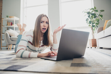 Fototapeta premium Young woman indoors puzzled while using laptop in living room during the day, relaxing at home, expressing confusion or frustration.