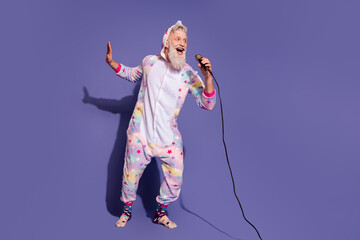 Joyful mature man in a colorful unicorn onesie singing and having fun against a vibrant purple backdrop