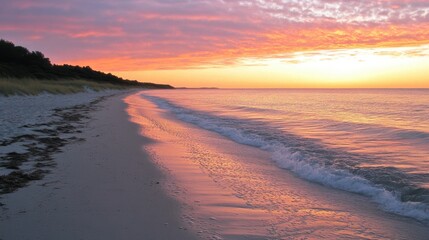 Serene sunrise over a sandy beach with gentle waves and a line of trees in the background.
