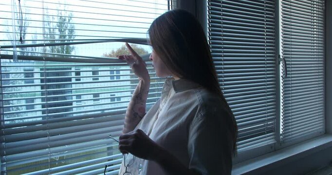 Beautiful sexy Girl aproaching the windows and looking though the window blind. Medium close up