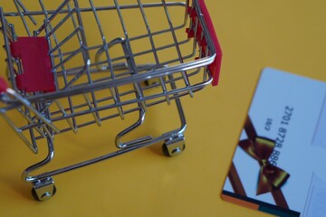 shopping concept. shopping cart with credit card with gift bow on yellow background