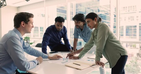 Friendly office workers stand at table in modern office engaged in discussion, brainstorm collaborate on process flowchart. Diverse businesspeople share ideas, planning strategy for business success - Powered by Adobe