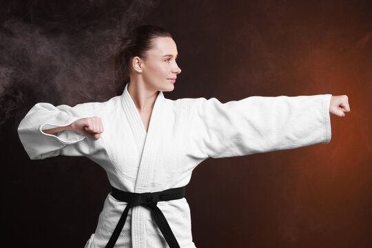 Young woman in kimono practicing karate on dark background