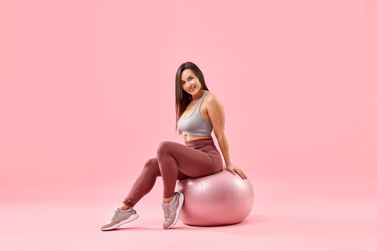 Woman in gym clothes with fitness ball on pink background