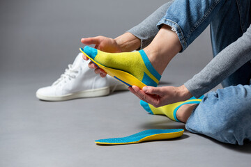 Close up of  female  hands fitting orthopedic insoles on a gray background.