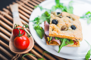 Italian sandwich made with focaccia bread, olives, ham, tomatoes 