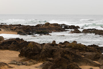 Stormy Ocean Waves Crashing Against Rocks with a Lighthouse in the Background