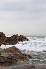 Stormy Ocean Waves Crashing Against Rocks with a Lighthouse in the Background