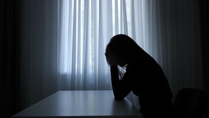 Silhouette of woman sitting at table in front of window. lays head on desk, depressed heartbroken...